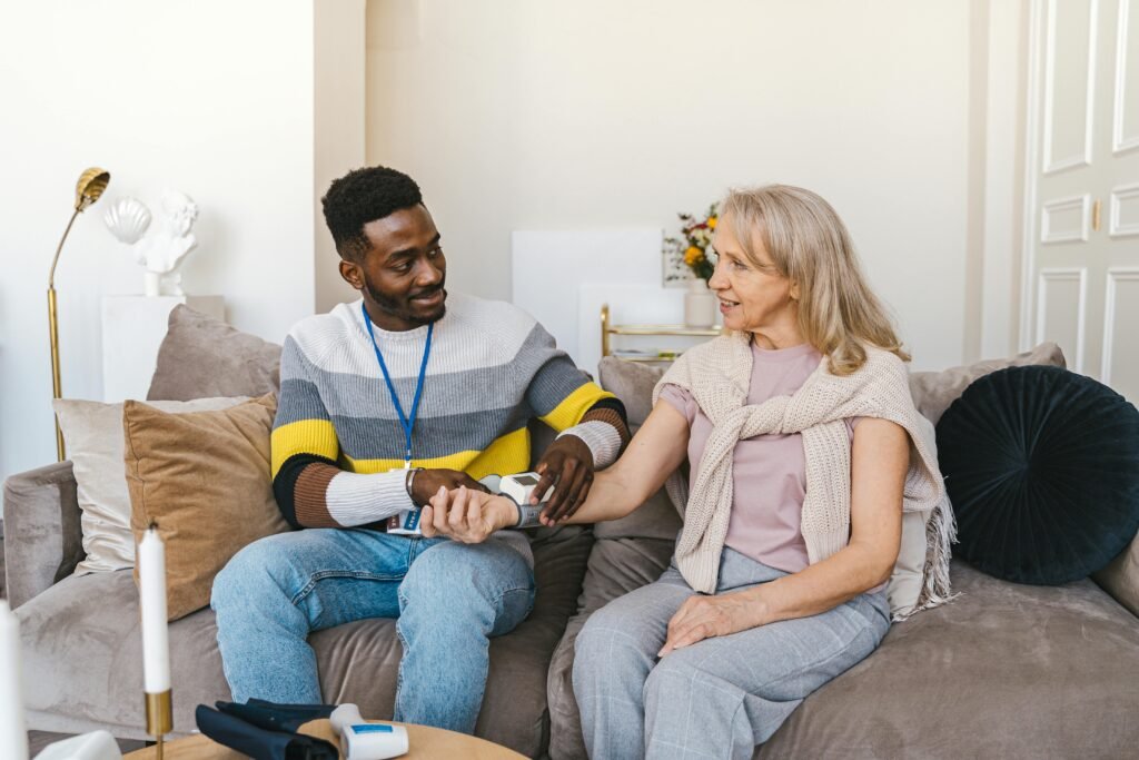 A volunteer checks the blood pressure of a smiling elderly woman indoors, showcasing care and support.